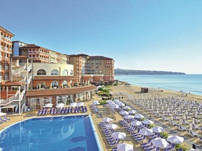 Beachfront hotel with pool, sun loungers, umbrellas, and ocean view under clear sky.