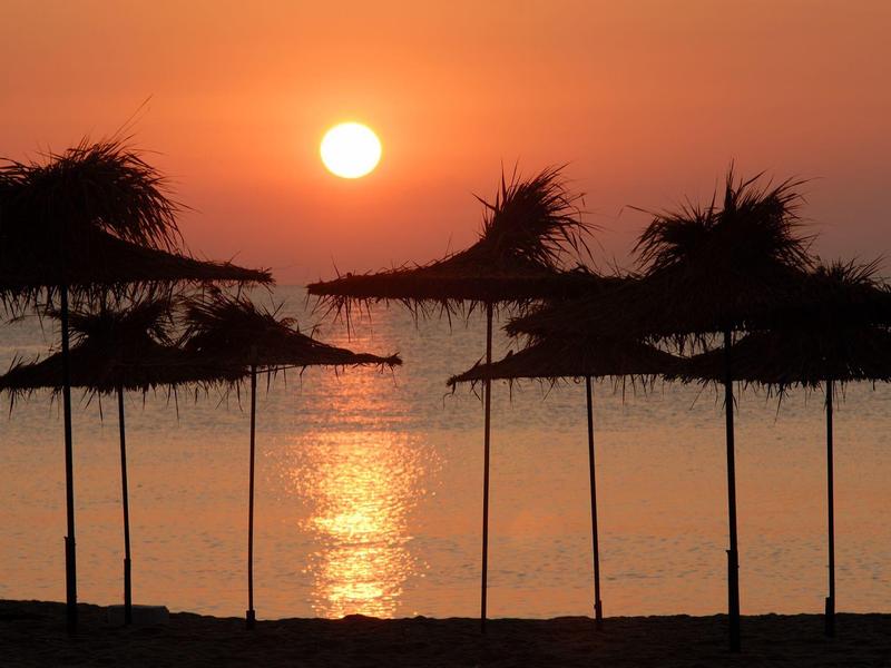 Sunset on the beach with straw umbrellas and calm water.