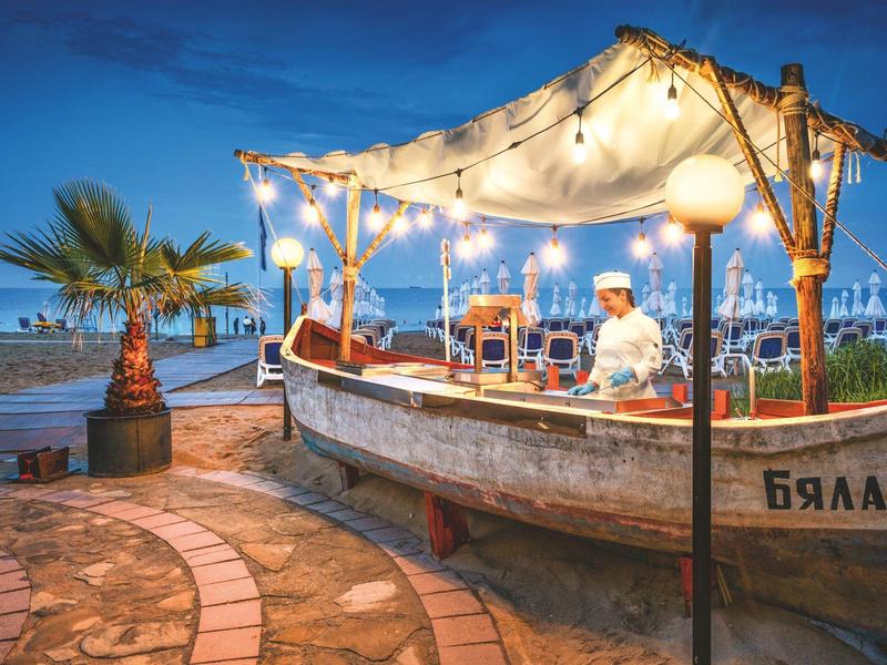Beach bar in a converted boat at sunset with string lights and palm trees