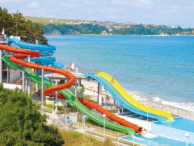 Colorful water slides at the beach with sea and green trees in the background.