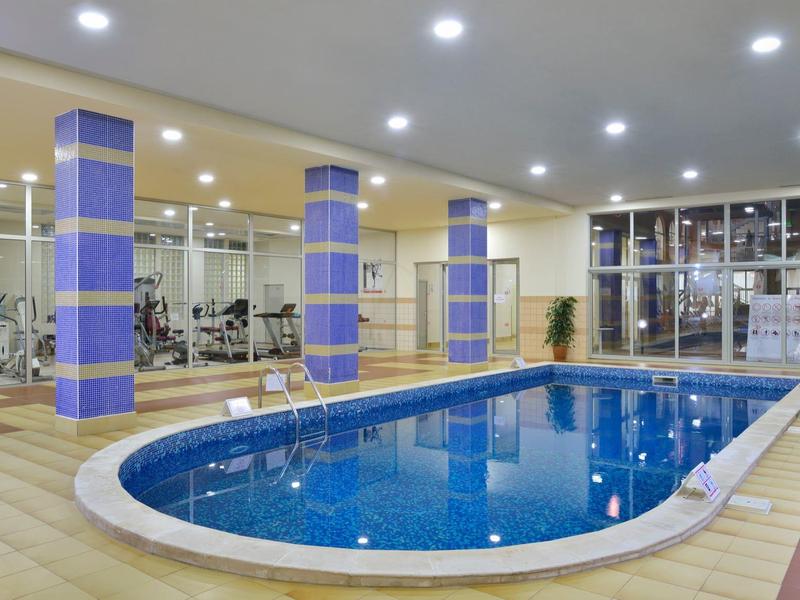 Indoor pool in a well-lit fitness area with glass walls and blue pillars.
