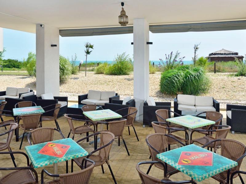 Open hotel terrace with tables and chairs, view of sand and sea in the background.