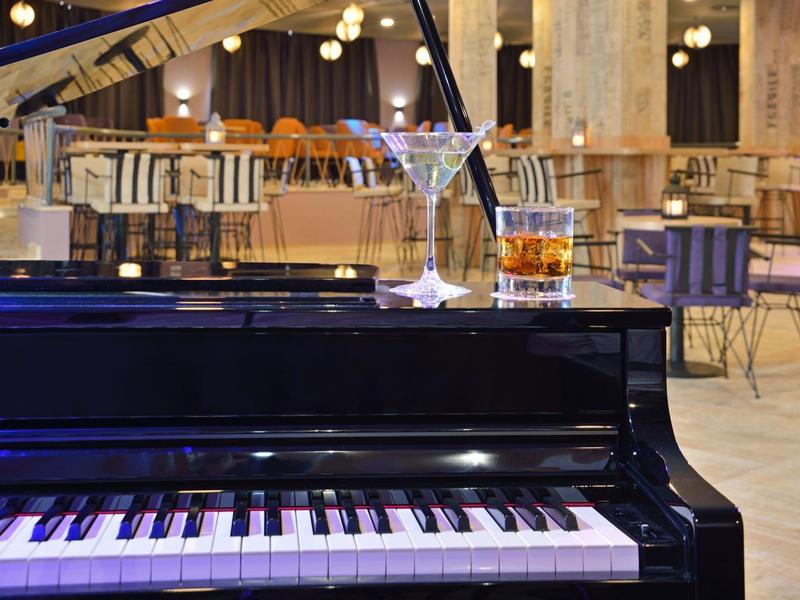 Black piano with two cocktails in a stylish bar setting in the background.