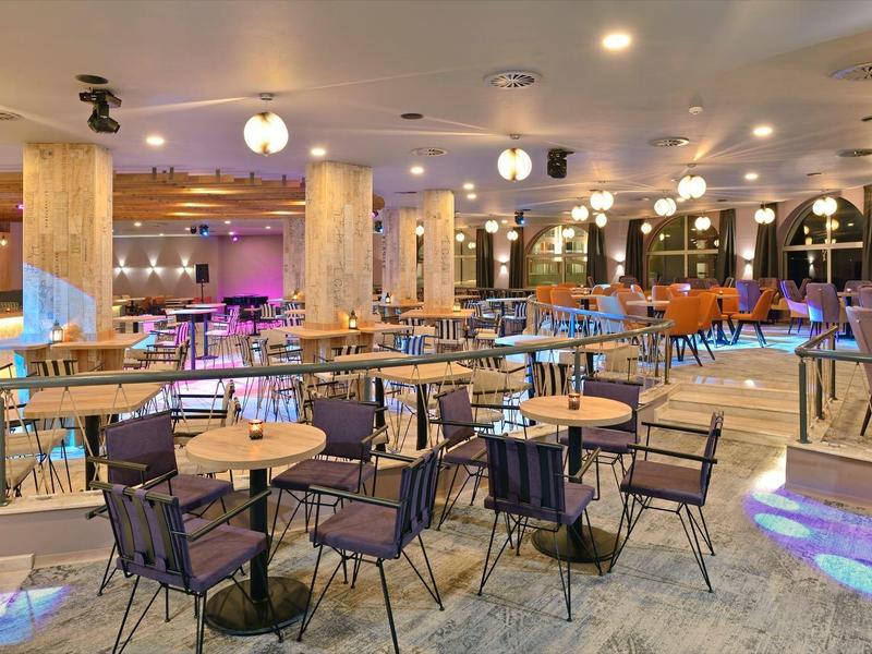 Bright, modern hotel restaurant with wooden tables and chairs on marble tile floor.