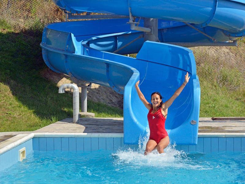 Woman in red swimsuit happily slides down blue water slide into swimming pool