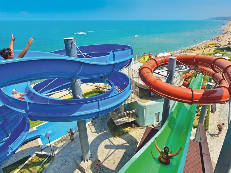 Water slides in a water park with sea view and people sliding.