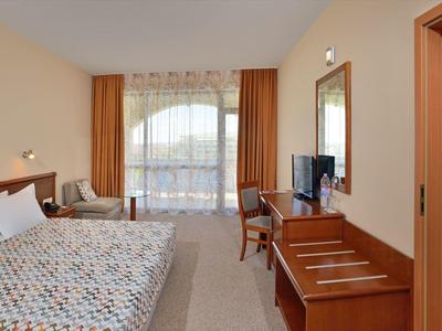 Hotelzimmer mit großem Bett, Schreibtisch, Fernseher, Stuhl und Fenster mit Vorhängen.