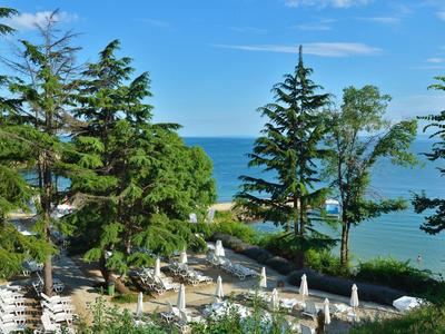 Grüner Garten mit weißen Sonnenschirmen und Blick auf das blaue Meer unter blauem Himmel.