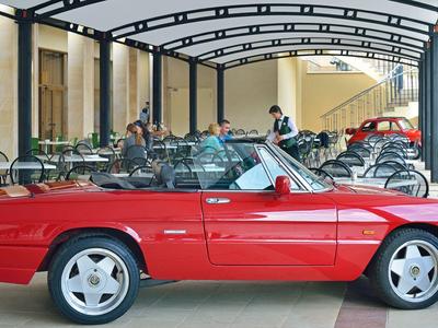 Rotes Cabrio mit geöffnetem Verdeck, grauen Sitzen, steht unter einem schwarzen Metallvordach.
