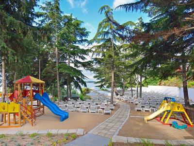 Spielplatz mit Rutschen, Klettergeräten und Bänken in einem bewaldeten Strandbereich.