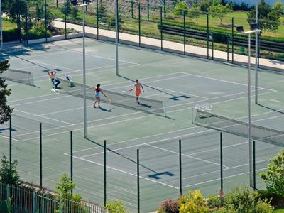 Tennisplatz mit zwei Spielern, umgeben von hohen Zäunen und grünem Bereich.