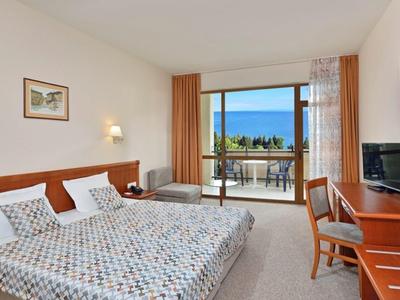 Helles Hotelzimmer mit Doppel- und Einzelbett, Holzmöbeln, Balkon und Meerblick.