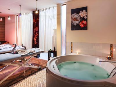 Moderner Wellnessraum mit Whirlpool, Massageliegen, Holz- und warmen Farbtönen, entspanntem Ambiente.