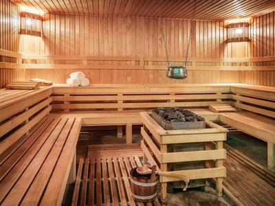 Holzsauna mit Sitzbänken, Saunaofen, Holzeimer und warmem Licht an den Wänden.