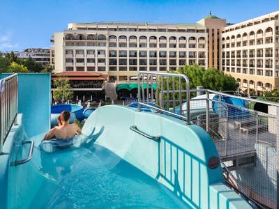 Ein Mann rutscht eine blaue Wasserrutsche neben einem großen Hotelgebäude bei klarem Himmel hinab.