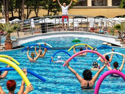 Menschen im Pool halten bunte Schwimmnudeln, Trainer macht Bewegungen am Beckenrand.