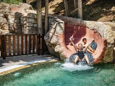 Zwei Personen kommen lachend auf einer Wasserrutsche ins grüne Wasser eines Freizeitparks.