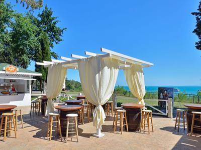 Offener Außenbereich mit Tischen und Stühlen unter weißen Baldachinen nahe Strand und Meer.