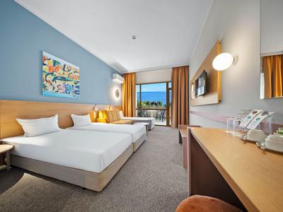 Camera d'hotel luminosa con letto matrimoniale, scrivania, balcone e arredamento moderno.