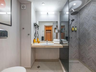 Modernes Hotelbad mit Waschtisch, Spiegel, Haartrockner und begehbarer Dusche mit Glaswand.