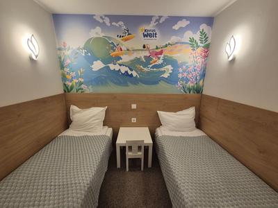 Kleines Hotelzimmer mit zwei Einzelbetten, Nachttisch und einer bunten Wandmalerei.