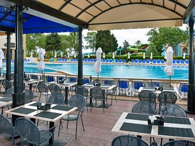 Outdoor-Café mit Tischen, Stühlen und Blick auf ein großes Schwimmbecken unter blauem Himmel.