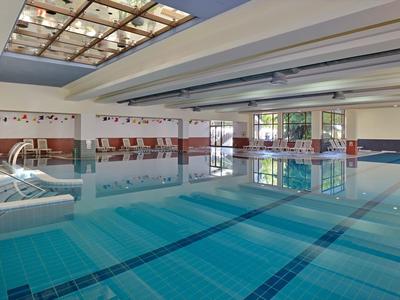 Innen-Schwimmbad mit klarem Wasser, blauen Fliesen und hellem Glasdach, umgeben von weißen Wänden.