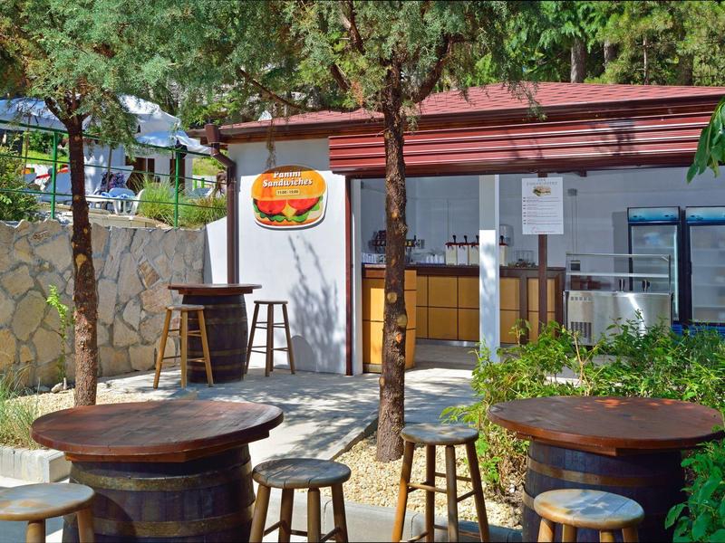 Accogliente area esterna di un bar con tavoli in legno e mobili da barili di vino sotto gli alberi.