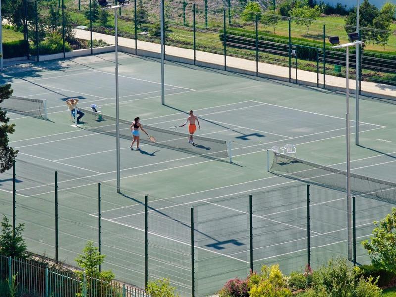 Due persone giocano a tennis su un campo da tennis all'aperto con recinzione verde.