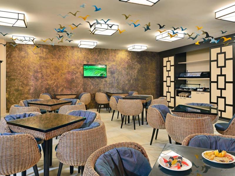 Area lounge accogliente in hotel con poltrone in vimini, tavoli e illuminazione moderna.