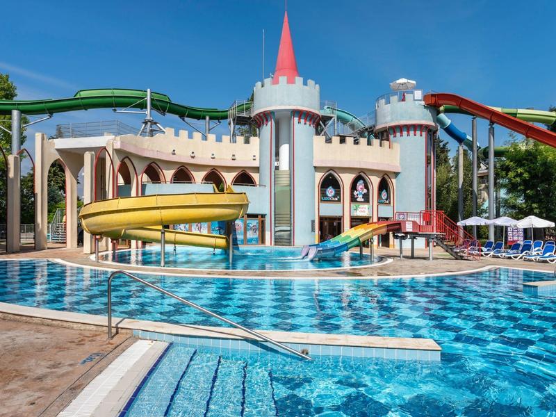 Parco acquatico con piscina, scivoli d'acqua e un edificio a forma di castello sullo sfondo