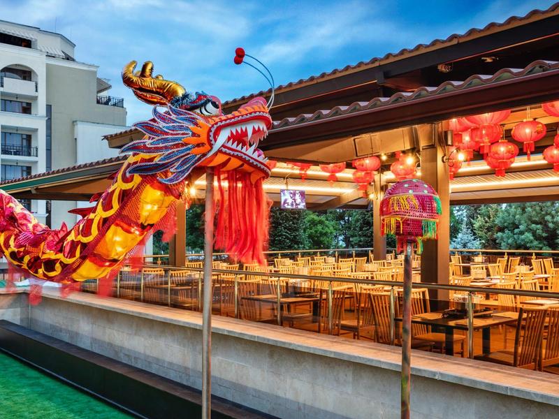 Decorazione di drago cinese colorata davanti a un ristorante tradizionale coperto con tavoli di legno e lanterne rosse.