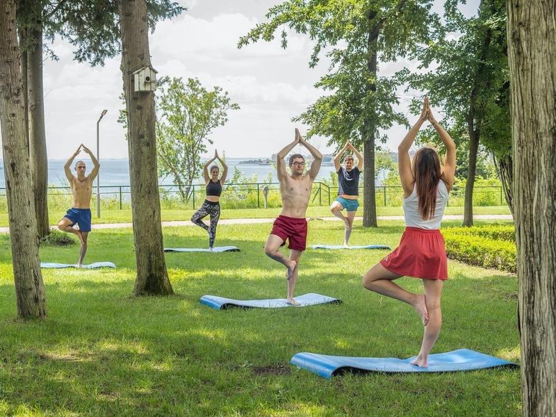Diverse persone praticano yoga all'aperto in un parco con vista su un lago.