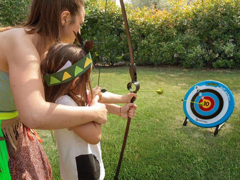 Una donna insegna a un bambino a tirare con l'arco su un bersaglio nel giardino.