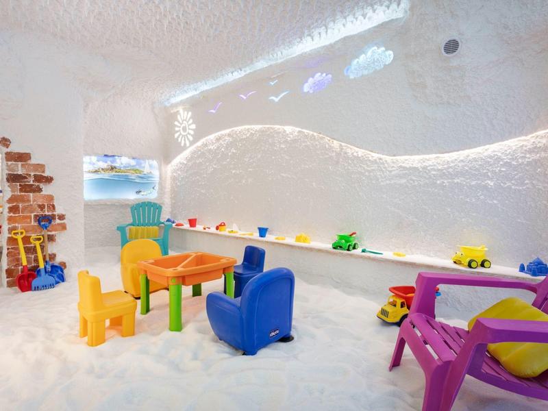 Sala giochi per bambini con mobili colorati e giocattoli in una stanza bianca.