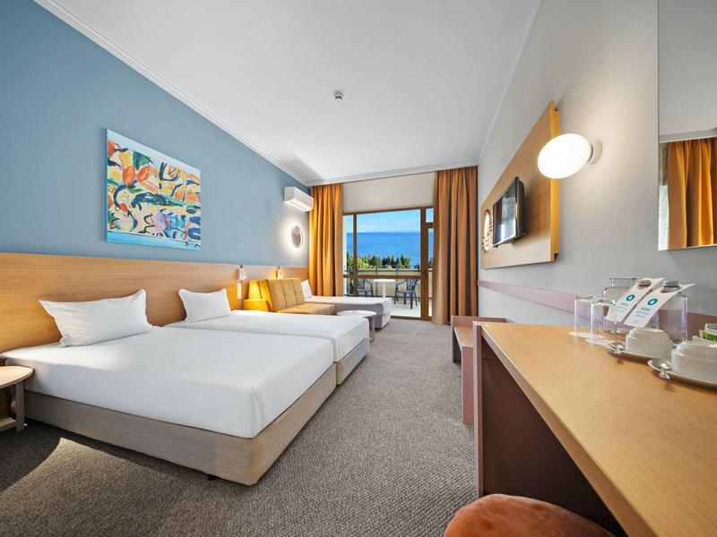 Camera d'hotel luminosa con letto matrimoniale, scrivania, balcone e arredamento moderno.