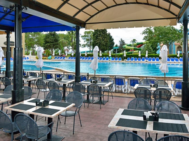 Terrazza esterna coperta con tavoli e sedie accanto a una grande piscina.