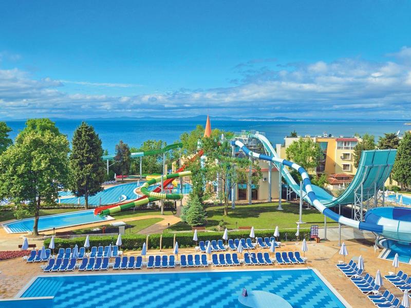Grande piscina all'aperto con cascate, scivolo d'acqua e lettini con vista sul lago e colline boschive.