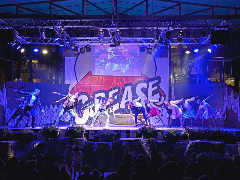 Gruppo di ballerini si esibisce sul palco davanti a uno sfondo Grease di notte.
