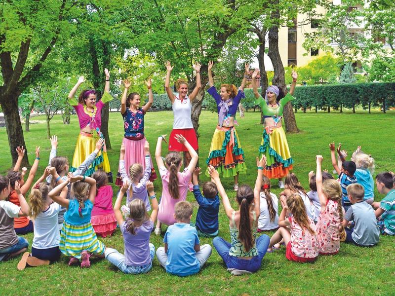 Gruppo di bambini che ballano e applaudono in cerchio su un prato verde nel parco.