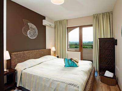 Kleines, gemütliches Schlafzimmer mit Doppelbett, brauner Wand, grünem Vorhang und Balkon.