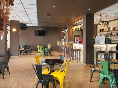 Moderner Hotelbarbereich mit Holztresen, bunten Stühlen und Frühstückstischen.