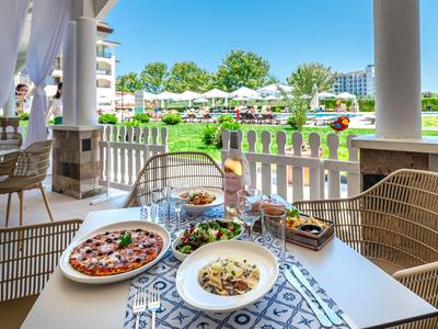 Esstisch mit italienischem Essen auf einer Terrasse mit Blick auf gepflegte Gärten und Hotelgebäude.