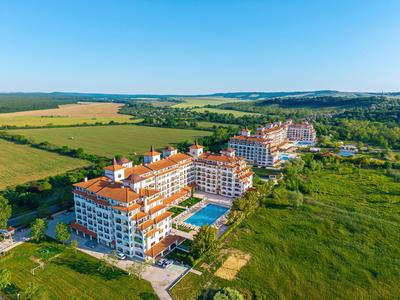 Großes Hotel mit Pools in grüner, ländlicher Umgebung unter blauem Himmel.