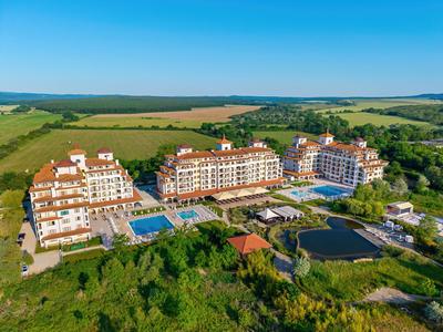 Große Hotelanlage mit Pools zwischen grüner Landschaft und Feldern unter klarem Himmel.