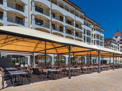 Hotelterrasse mit gedeckten Tischen und Stühlen vor einem weißen, mehrstöckigen Gebäude bei klarem Himmel.