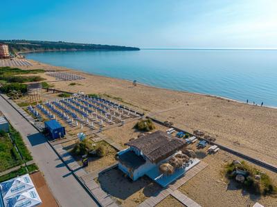 Blick auf einen ruhigen Sandstrand mit Reihen von Sonnenliegen und einem kleinen Strandkiosk bei klarem Himmel.