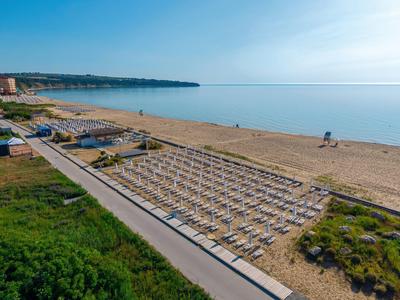 Weite Strandpromenade mit Reihen von Sonnenliegen und ruhigem, blauem Meer im Hintergrund.