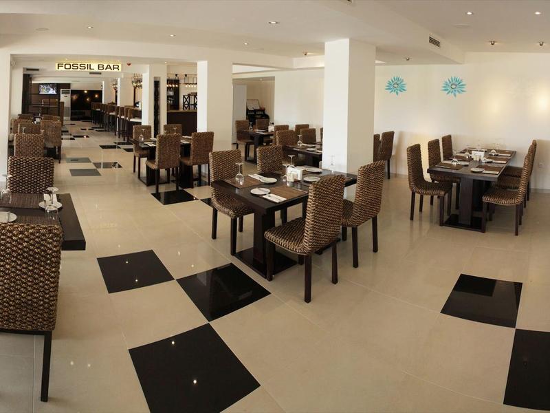Spacious, bright dining room with many tables and chairs and black and white floor tiles.