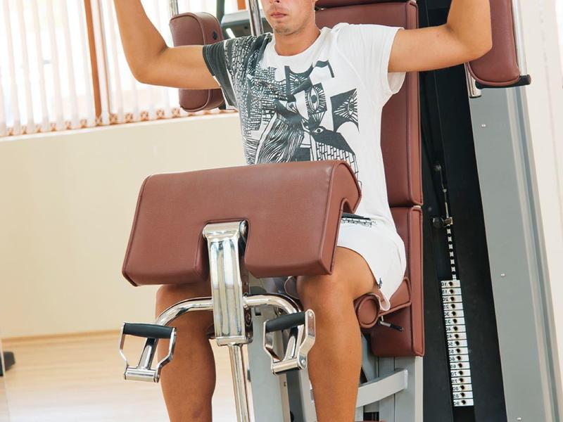 Boy works out on exercise machine in well-lit room with wooden floor.